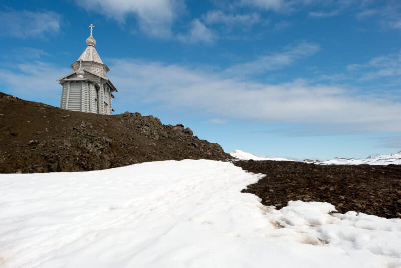 Trinity Church with onion dome, gilded cross and log walls on rocky hill above Bellingshausen Station, King George Island