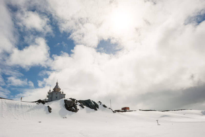Trinity Church with log walls, onion dome and gilded cross on rocky hill above Bellingshausen Station, King George Island