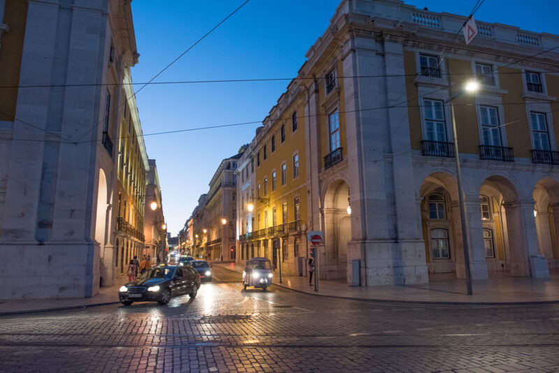 Quiet stone-paved sidestreet off Praça do Comércio lined with Pombaline facades and iron balconies at dusk