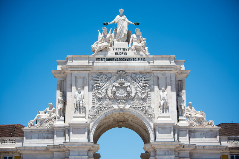 Facade of the Arco da Rua Augusta with its crest, statues, and crowning sculptural group under a clear sky