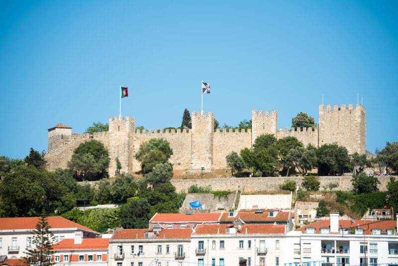 Castelo de São Jorge's crenellated stone walls and flags crown a hill above Lisbon's Alfama rooftops