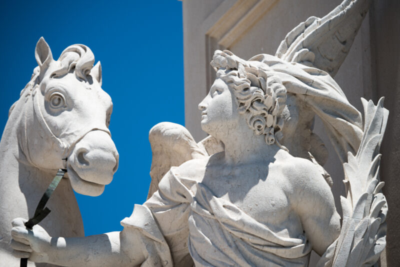 Close-up of a winged allegorical figure and horse carved atop the Arco da Rua Augusta