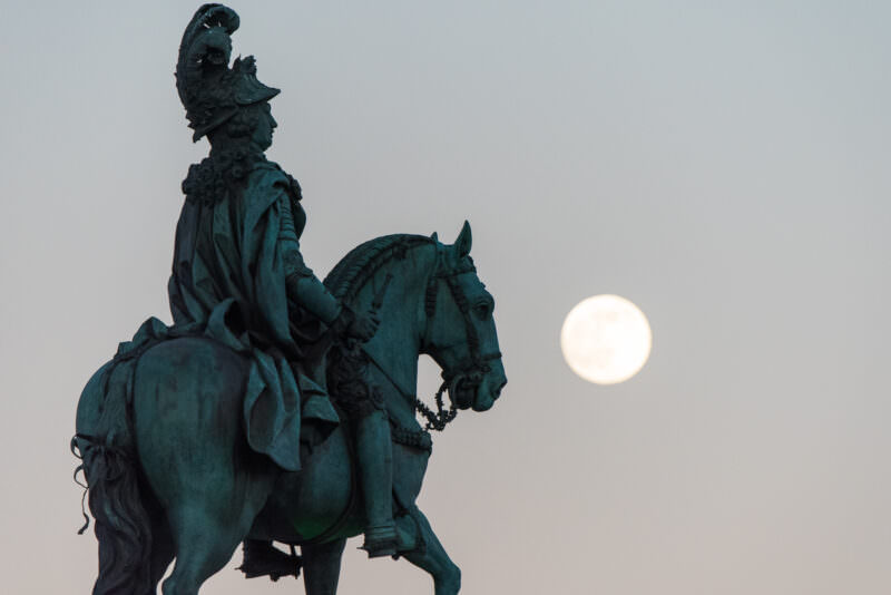 King Joseph I's bronze equestrian statue in profile against a rising full moon in Lisbon