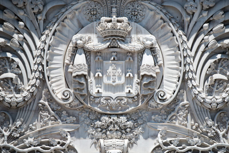 Carved Portuguese coat of arms in ornate stone relief on the Arco da Rua Augusta facade