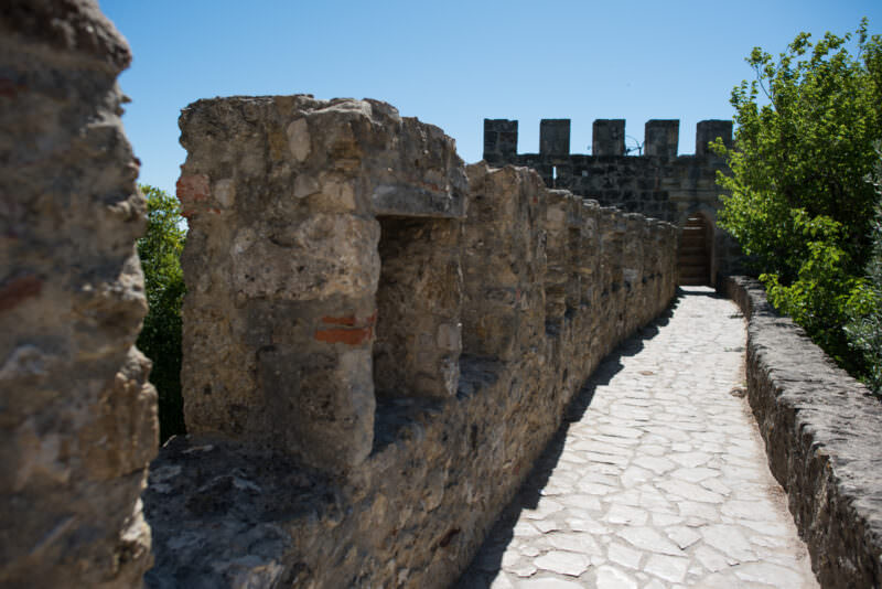 A stone pathway winds along the crenellated Moorish-era walls of Castelo de São Jorge