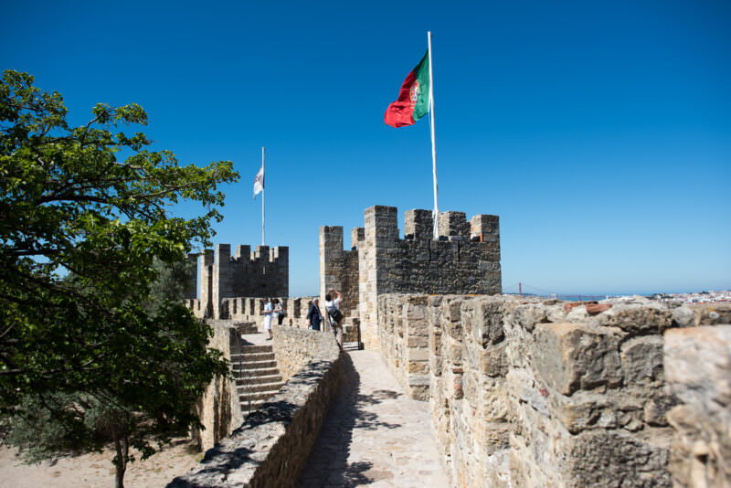 The Portuguese flag flies over a crenellated stone tower on the ramparts of Castelo de São Jorge