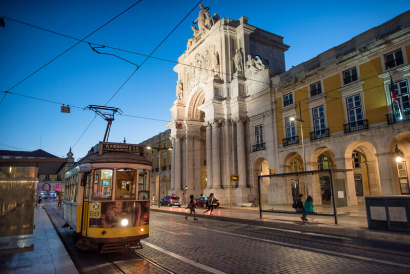 Yellow tram passing the illuminated Arco da Rua Augusta on Praça do Comércio at dusk
