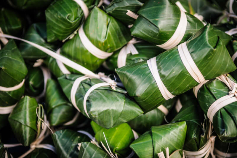 Fish parcels wrapped in banana leaves and tied with pale bamboo strips, stacked in a green pile