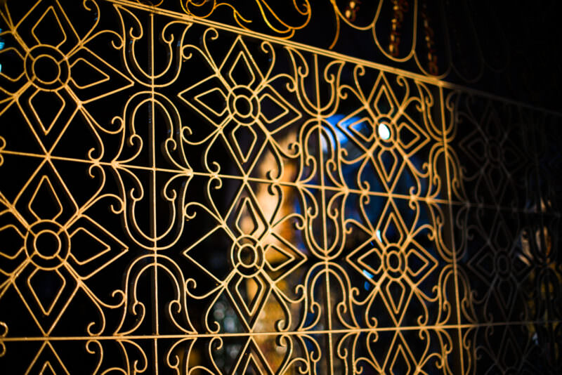 Gilded metalwork grille on Sutaungpyei Pagoda shrine door, diamond-and-scroll lattice screening lit Buddha figure beyond
