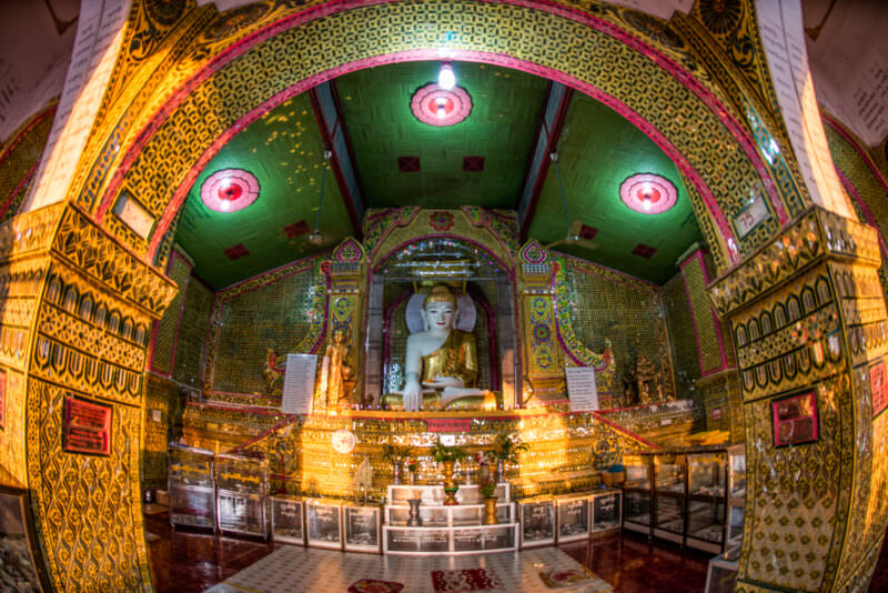 White Buddha in bhumisparsha mudra inside Sutaungpyei Pagoda, gold-and-green mirrored-glass mosaic covering walls and barrel-vaulted ceiling