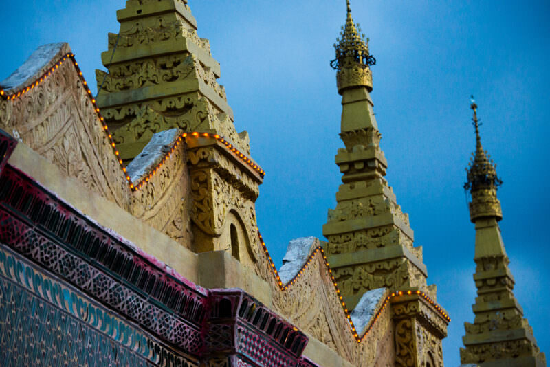 Gilded stucco spires above mirrored-glass eaves of Sutaungpyei Pagoda, electric light strings tracing roofline against twilight
