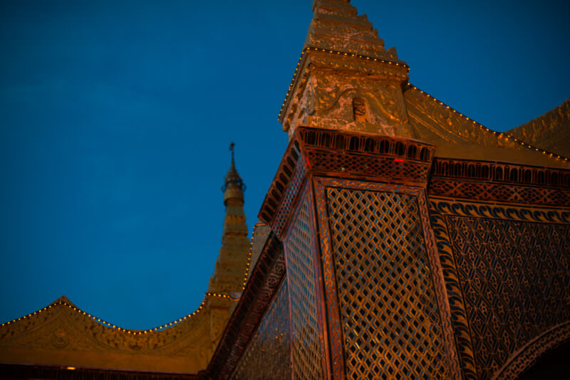 Mirrored-glass mosaic spire and tiered masonry of Sutaungpyei Pagoda under warm artificial light against deep-blue twilight sky