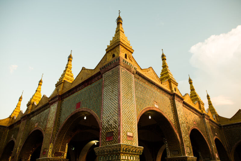 Mirrored-glass mosaic arched pavilions of Sutaungpyei Pagoda under daytime sky, golden stupas and decorative spires above