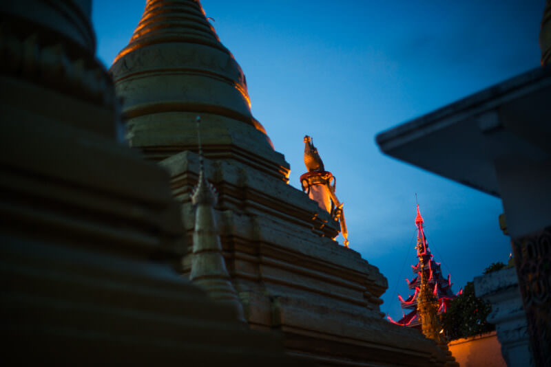 Gilded stupas and red-neon-lit pyatthat spire of Sutaungpyei Pagoda glowing against blue-hour sky atop Mandalay Hill