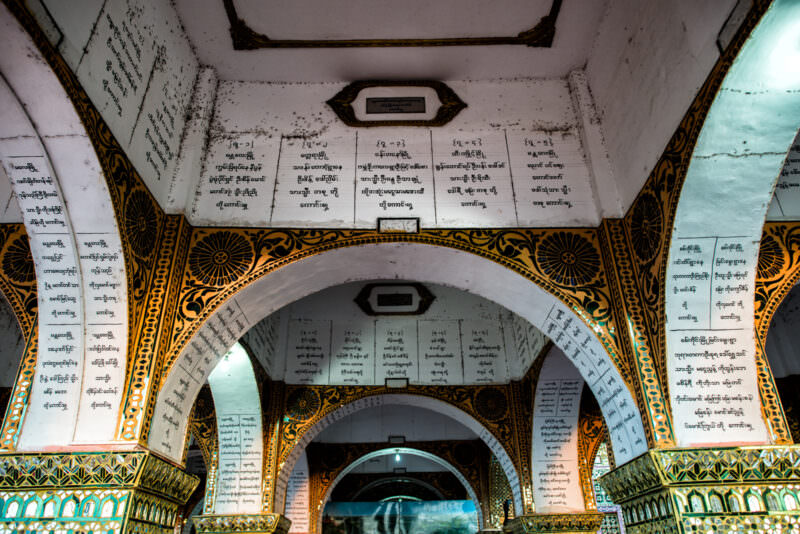 Burmese-script donor tablets plastering vaulted ceiling and arched bays of Sutaungpyei Pagoda portico, white stone recording benefactors