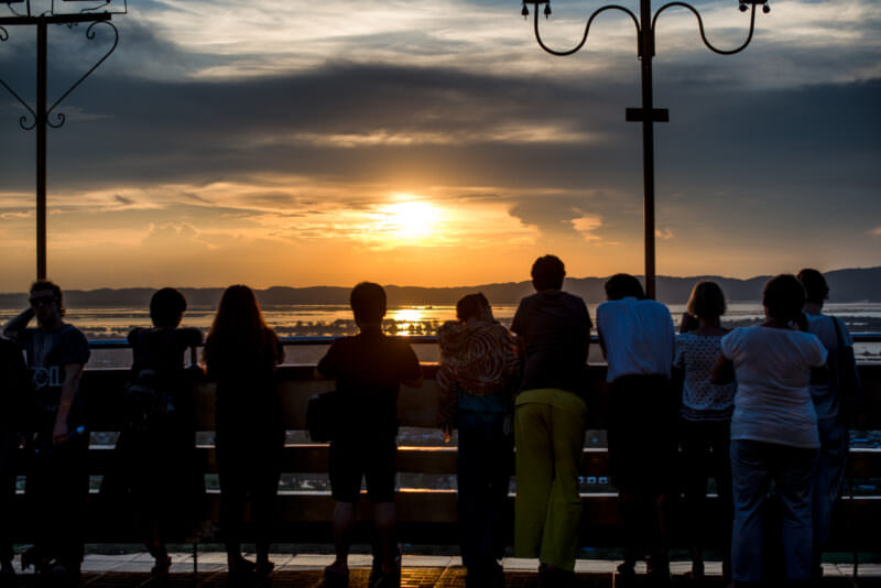 Visitors silhouetted along open terrace of Sutaungpyei Pagoda at sunset, Ayeyarwady River gleaming across plain below