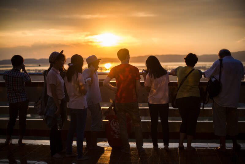 Visitors silhouetted against Ayeyarwady River sunset from Sutaungpyei Pagoda terrace, golden light streaming across plain below