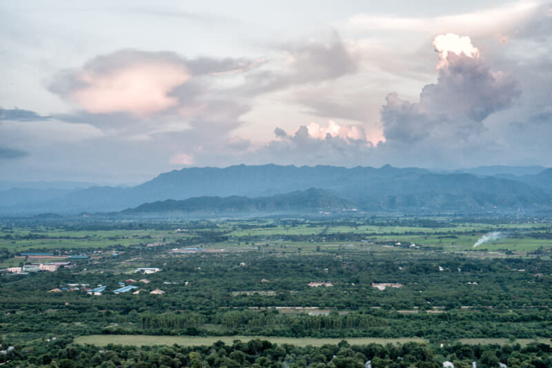 Mandalay Plain spreading toward distant Shan Hills viewed from Mandalay Hill summit, fields and settlements under clouded sky