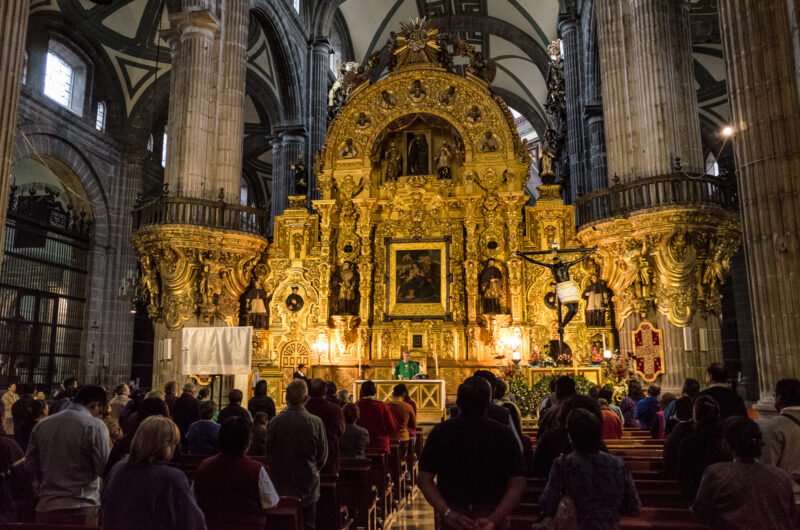 Congregation filling the nave during Mass, facing the gilded Altar del Perdón beneath the vaults