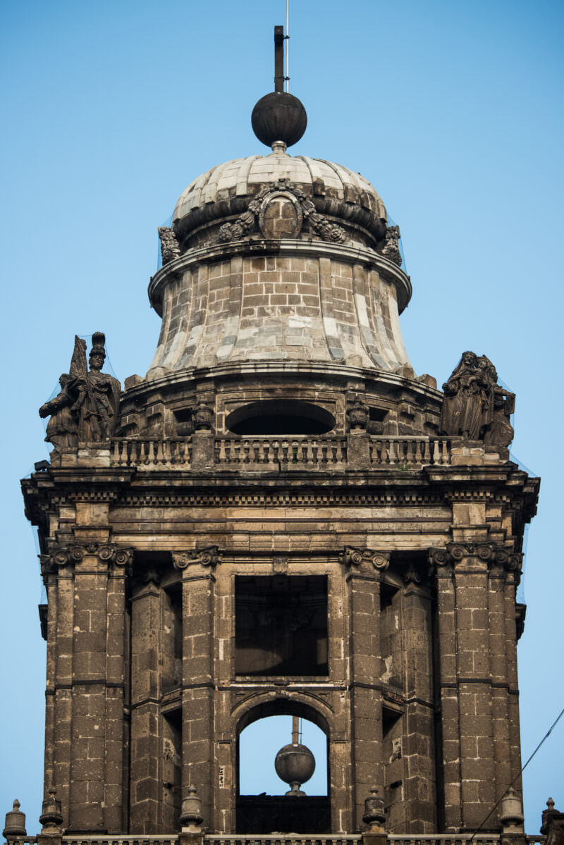 Bell tower rising to its bell-shaped crown, stone saints at corners, sphere-and-cross finial above