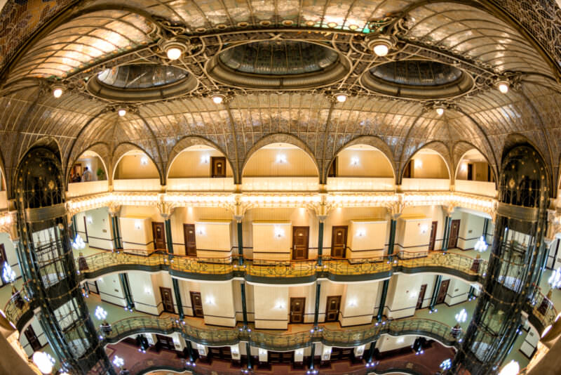 Multi-level atrium of Gran Hotel Ciudad de Mexico viewed from above, showing amber-toned stained glass vault and three oval skylights