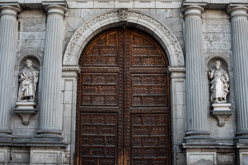 Studded wooden portal flanked by two chiluca-stone apostle figures at a lateral cathedral entrance