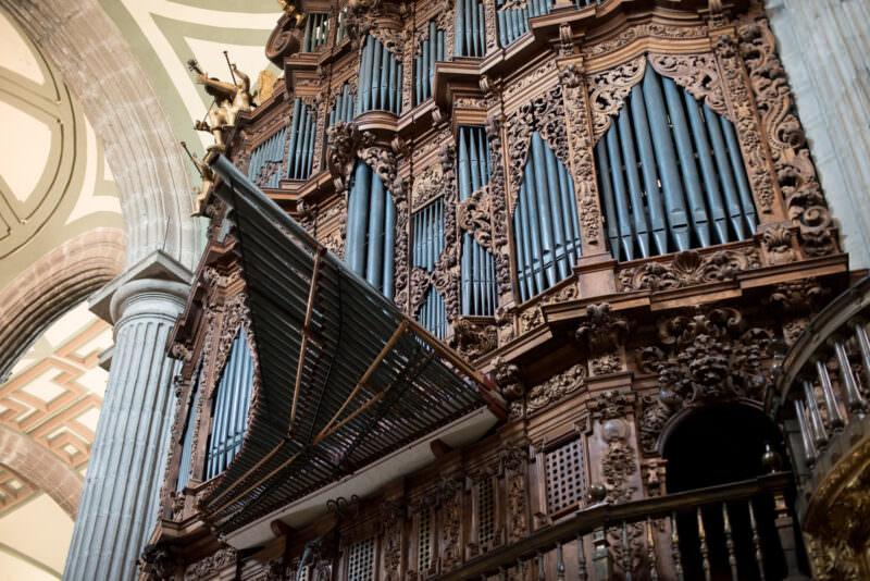 Monumental pipe organ rising above the nave, metal pipes behind Churrigueresque ornament and gilded angel