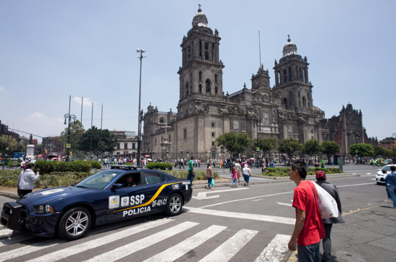Catedral Metropolitana's twin bell towers and Neoclassical dome across the Zócalo, police car in foreground