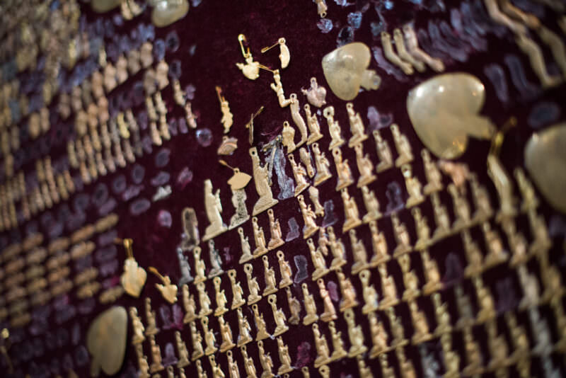 Hundreds of small metal milagro votive charms pressed into deep-red velvet around a sacred image
