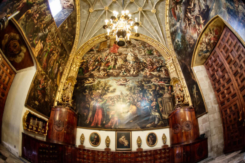 Sacristy apse wall covered by colonial oil paintings beneath a stellar ribbed vault and brass chandelier