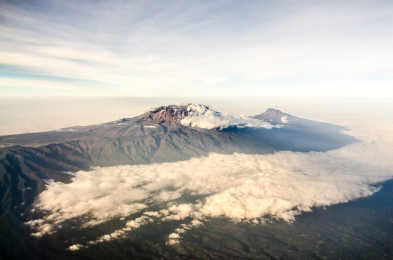 Aerial view of Kibo's snow-capped dome and jagged Mawenzi peak rising above clouds on Kilimanjaro