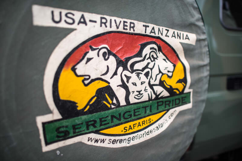 Serengeti Pride safari logo with three lions painted on a Land Cruiser's spare tire cover near Kilimanjaro