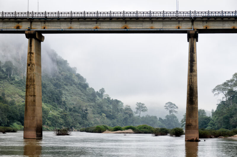 Tall concrete piers supporting Nong Khiaw's highway bridge over the Nam Ou, framed by misty limestone peaks