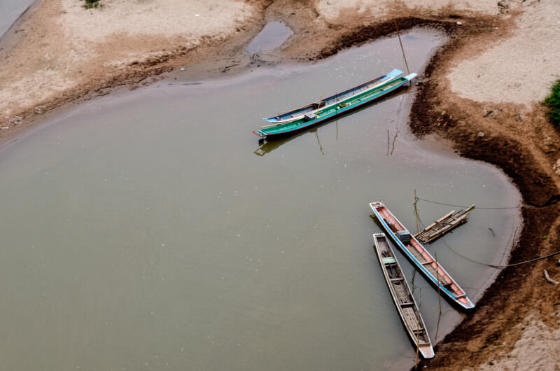 Narrow wooden canoes resting in a shallow sandy inlet along the Nam Ou, viewed from above during low water