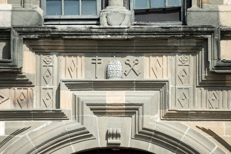 Carved stone lintel of the Catedral Metropolitana facade showing a papal tiara flanked by crossed keys, geometric borders, and decorative moldings