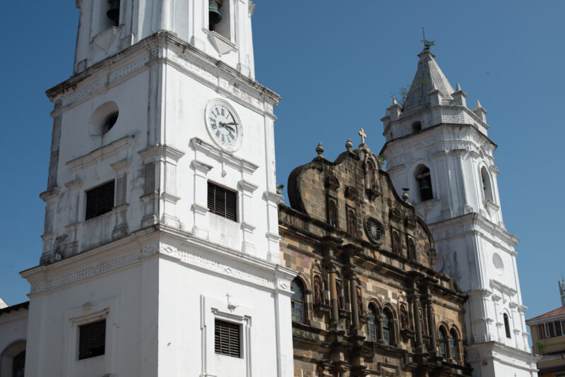 Catedral Metropolitana viewed from street level in Casco Viejo, one white bell tower at left and the weathered carved stone facade at center rising above adjacent buildings