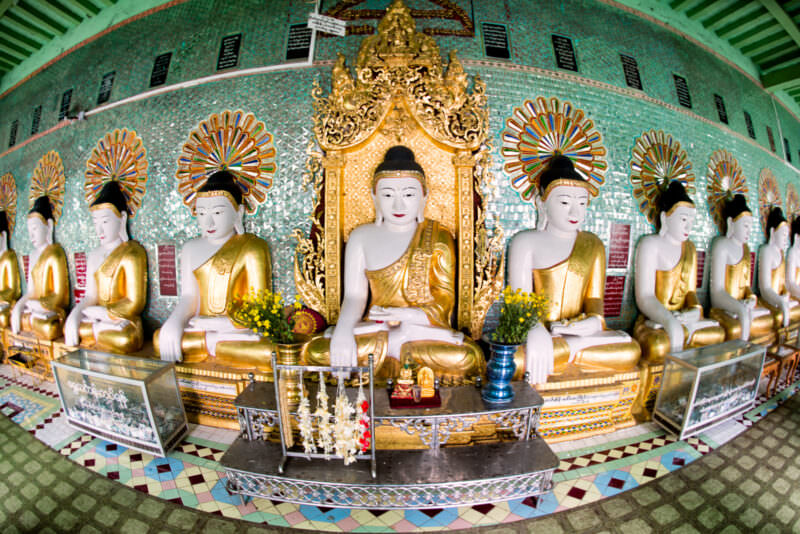 Forty-five gilded Buddha images seated in a crescent row against a turquoise glass-mosaic wall inside U Min Thonze Pagoda