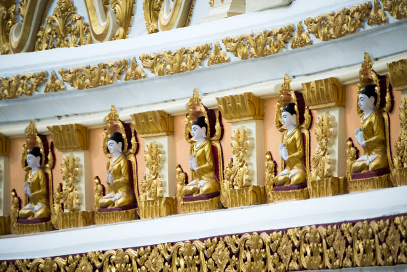 Gilded Buddha figures in individual stucco niches along the exterior arcade of U Min Thonze Pagoda on Sagaing Hill