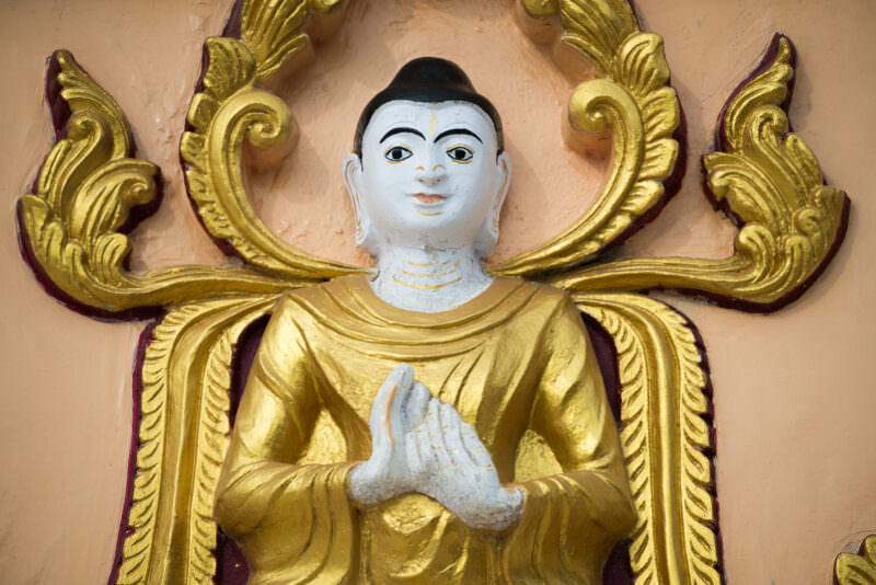 Gilded Buddha in anjali mudra with white face and gold robes, set in a stucco niche at U Min Thonze Pagoda