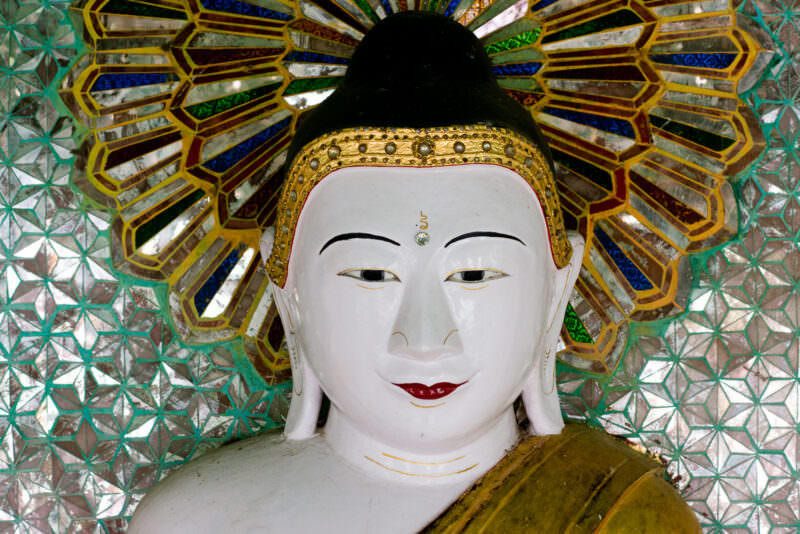 White-faced Buddha at U Min Thonze Pagoda framed by a radiating starburst of coloured and mirrored glass-mosaic