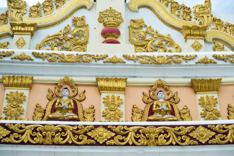 Gilded stucco relief of two white Buddha figures in ornate niches with dense floral scrollwork on U Min Thonze Pagoda's outer wall