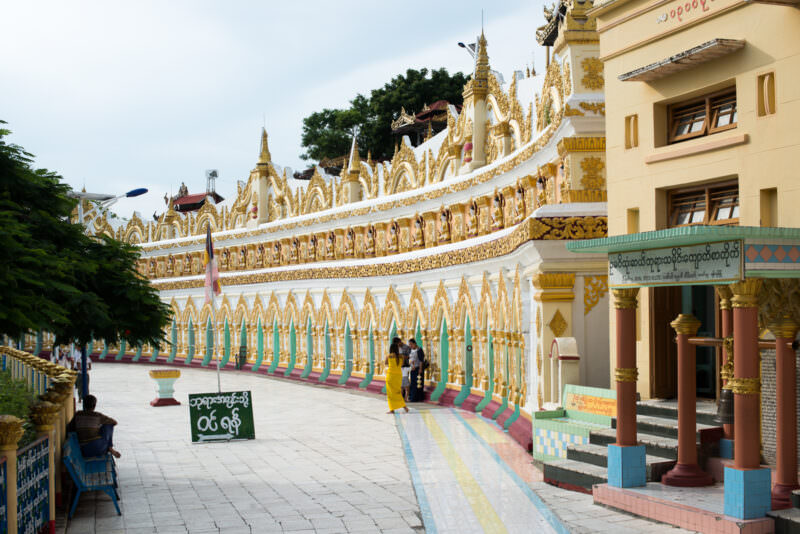 Visitors walking the forecourt of U Min Thonze Pagoda, its crescent facade of thirty gold-and-white arches stretching along Sagaing Hill