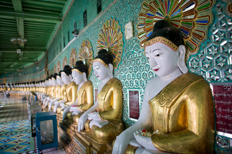 Forty-five gilded Buddha images receding in a crescent row, each backed by a glass-mosaic starburst at U Min Thonze Pagoda