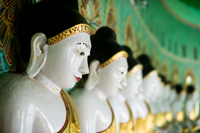 White-faced Buddha images with gold robes receding in profile along the curved inner wall of U Min Thonze Pagoda