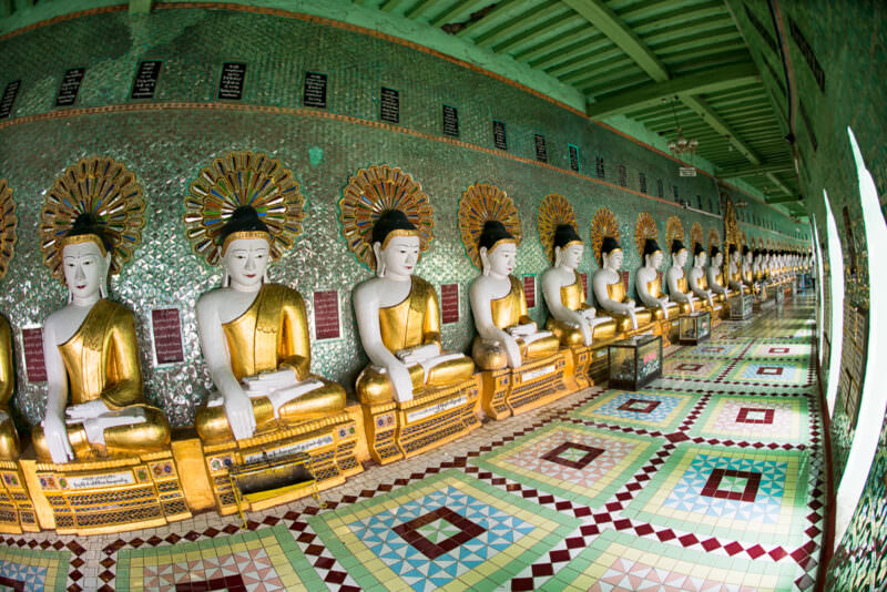 U Min Thonze Pagoda's full crescent colonnade with gilded Buddhas against turquoise glass-mosaic walls and geometric floor tiles