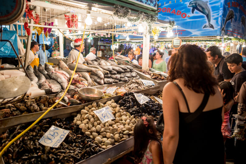 Brightly lit seafood stalls at Mercado Central with customers browsing large displays of fresh fish and bivalves at night