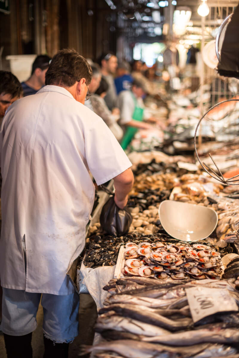 Vendor in white shirt preparing orders at seafood stall with scallops, mussels, and whole fish spread across display
