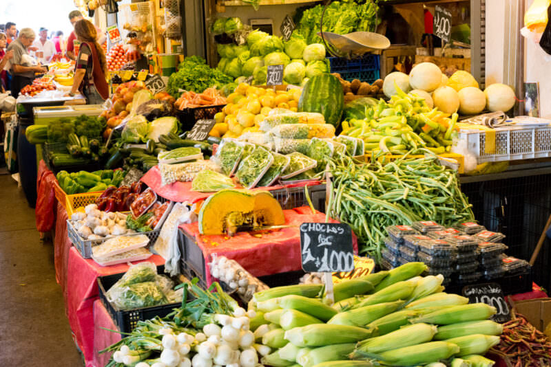 Produce stall at Mercado Tirso de Molina overflowing with corn, squash, melons, leafy greens, and other fresh vegetables
