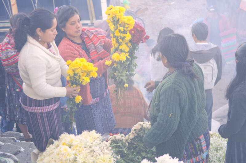 Flower vendors in traditional dress holding yellow blooms amid ceremonial smoke on Santo Tomas Church steps