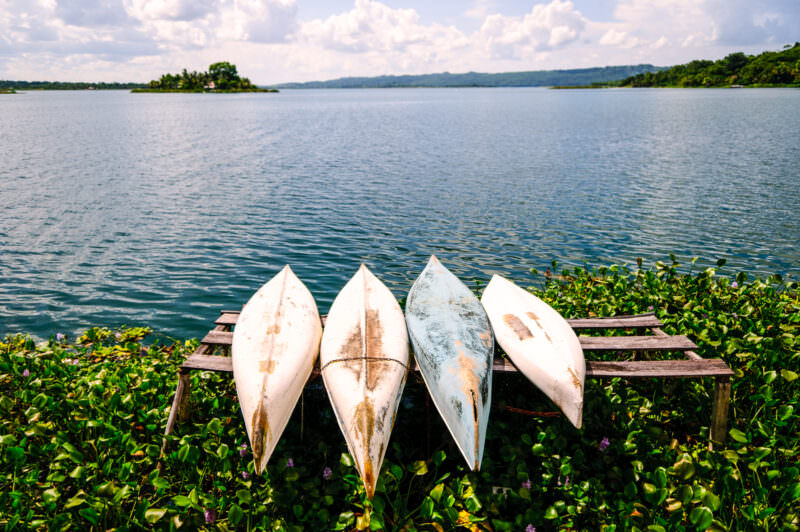 Four weathered white canoes resting upside down on a wooden dock in Lake Petén Itzá, with Radio Petén Island visible in the background